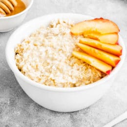 peaches and cream oatmeal with fresh peach slices in a white bowl. honey in the background