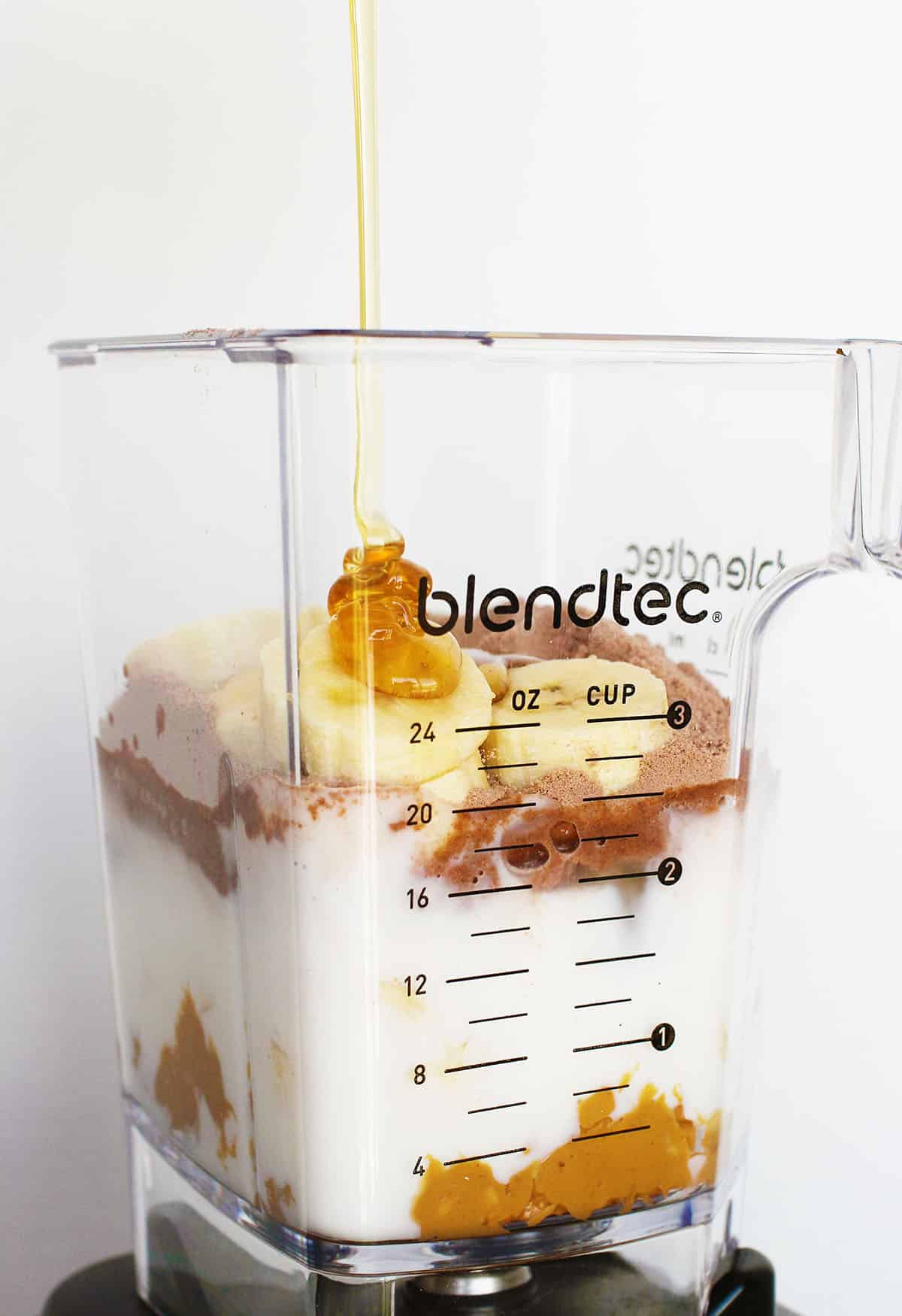 ingredients for peanut butter banana smoothie in a blender - milk, peanut butter, bananas, chocolate protein powder, honey.