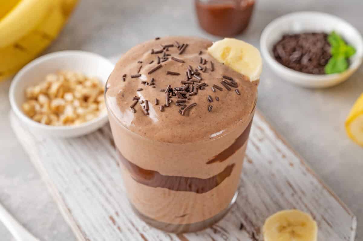 peanut butter banana smoothie with chocolate glaze and sprinkles in a glass on a gray concrete background. 