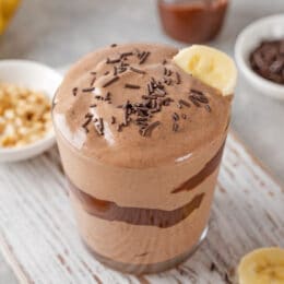 peanut butter banana smoothie with chocolate glaze and sprinkles in a glass on a gray concrete background.