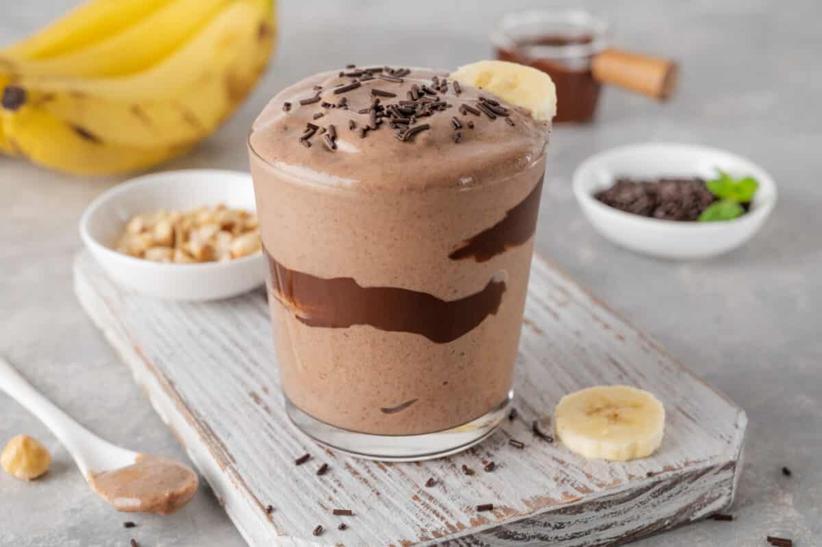 peanut butter banana smoothie with chocolate glaze and sprinkles in a glass on a gray concrete background.