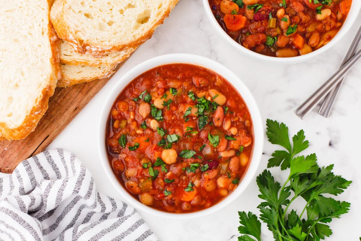 15 bean soup served in a white bowl with bread on the side.