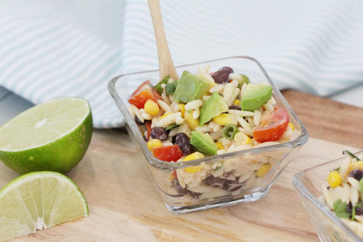 small glass bowl of avocado salad with a wooden spoon and lime slices