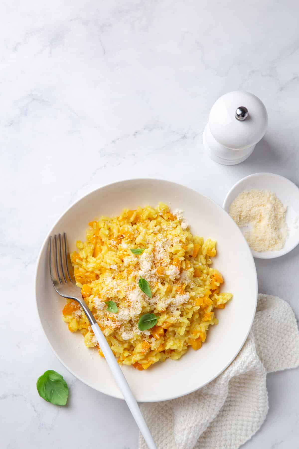 butternut squash in a white plate with a white pepper grinder on a marble countertop