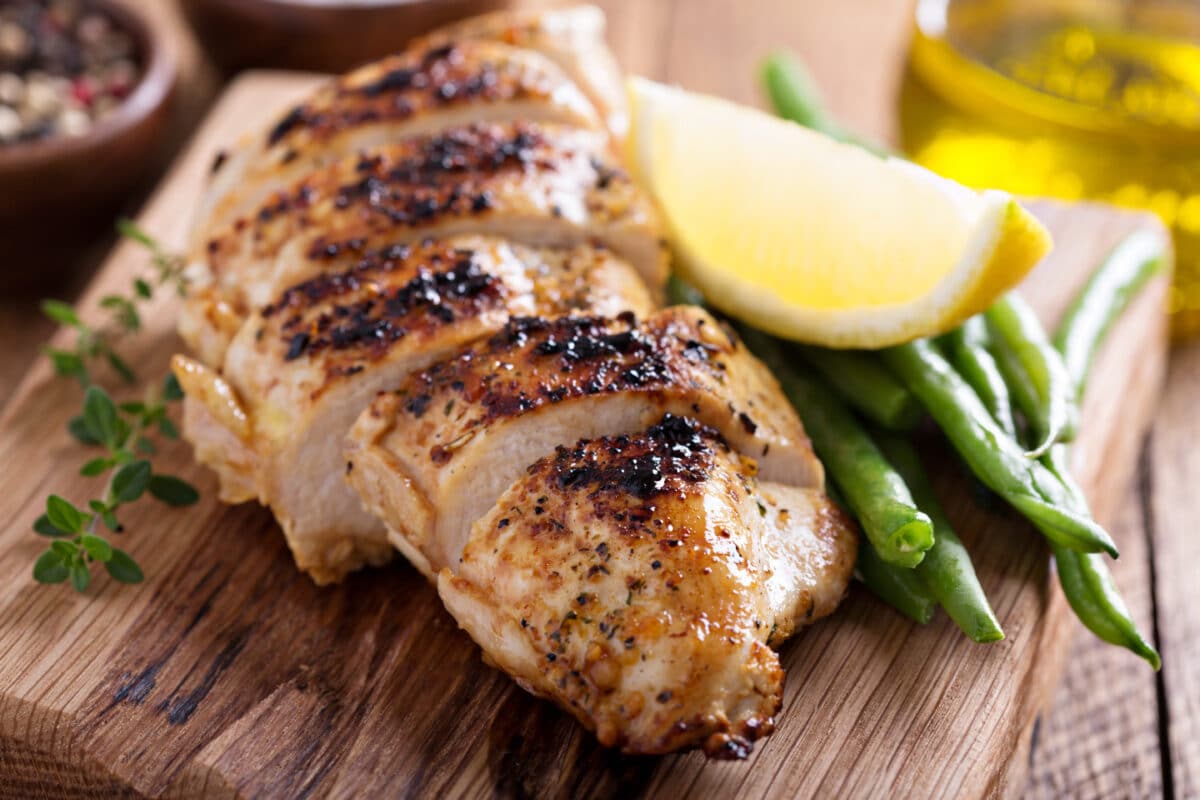 Grilled lemon chicken on a cutting board with thyme and green beans