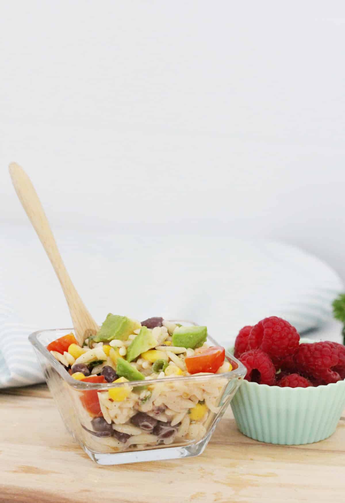 small bowl of avocado salad with a wooden spoon and served with raspberries