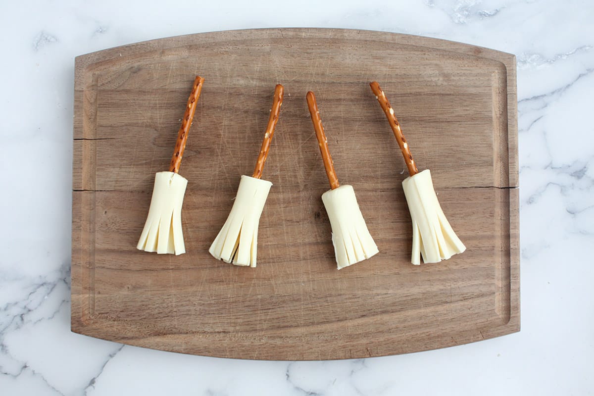 pretzel sticks inserted into string cheese to resemble brooms