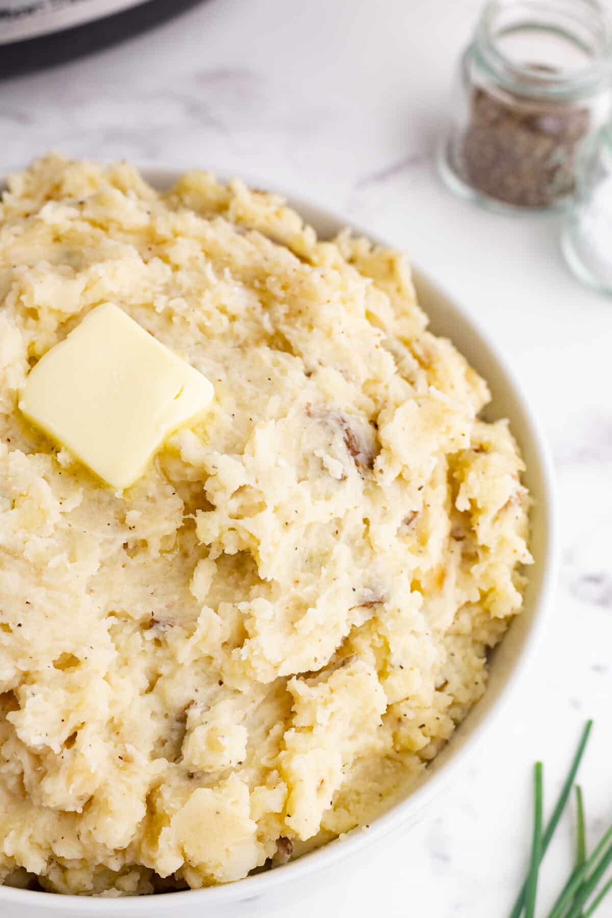 crockpot mashed potatoes in a white bowl with butter on top and green onion and black pepper in the background