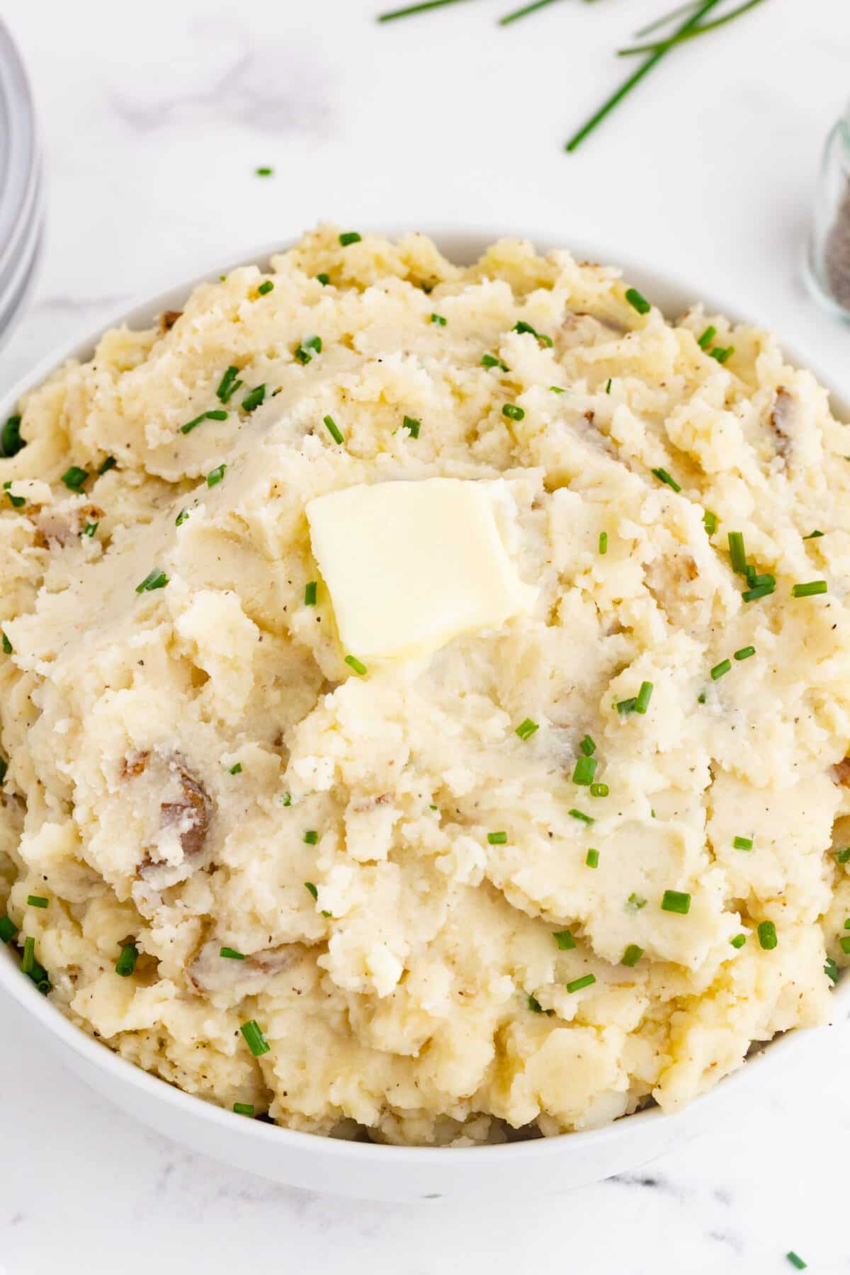 a bowl full of crockpot mashed potatoes with chives and a pat of butter on top