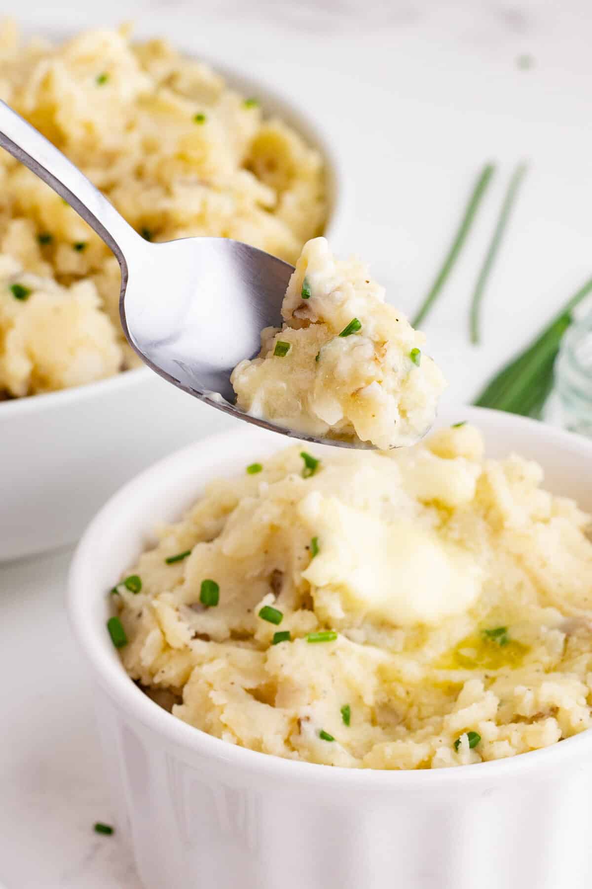 closeup of mashed potatoes being lifted on a spoon out of a white bowl with melted butter
