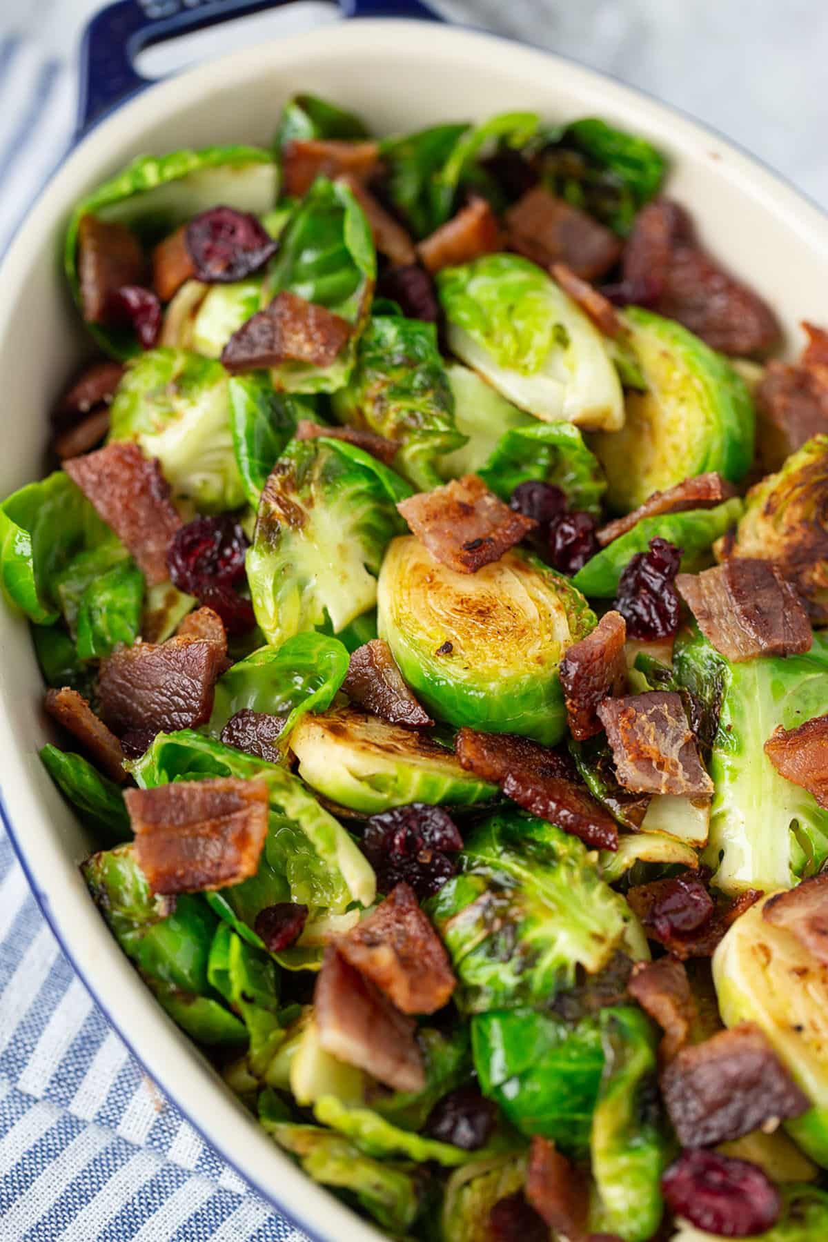roasted honey bacon brussels sprouts in a white dish with a blue and white linen in the background.