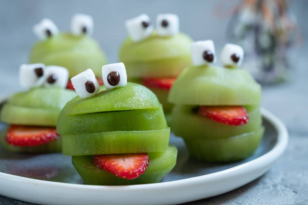 sliced kiwi stacked to resemble monsters with a strawberry tongue and marshmallow eyes