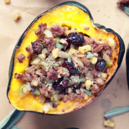 stuffed acorn squash with sausage, cranberries, sage, celery on a baking sheet with parchment paper