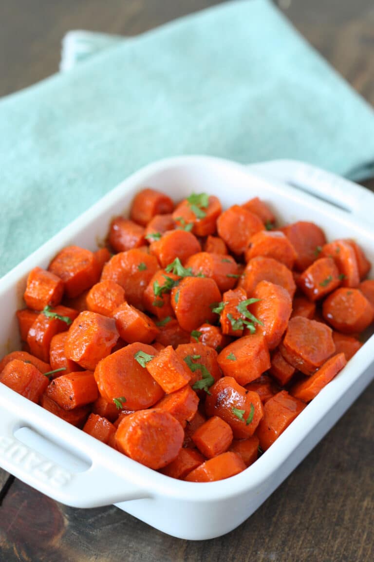 Roasted honey glazed carrots in a white casserole dish with a blue linen backdrop