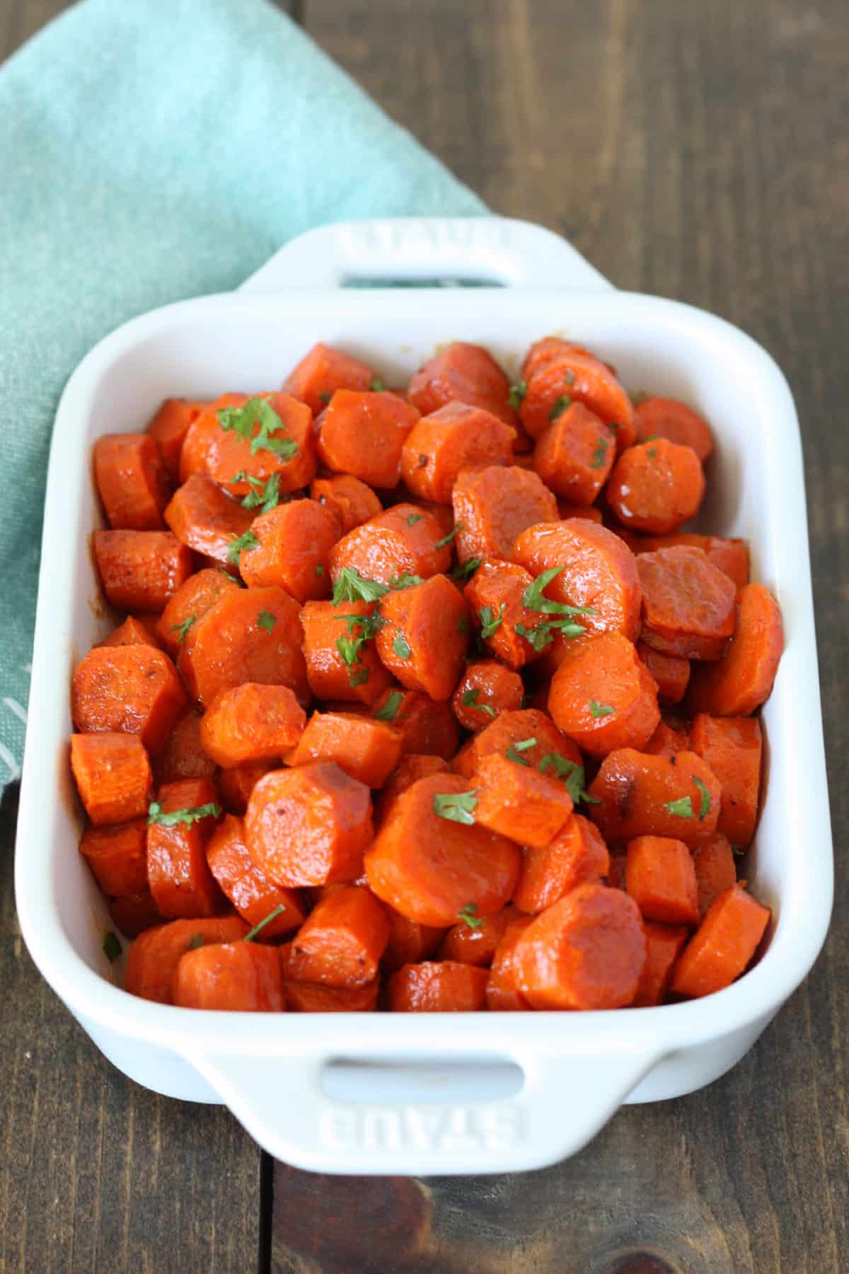 honey glazed carrots cut into coins in a white baking dish with green parsley garnish on top