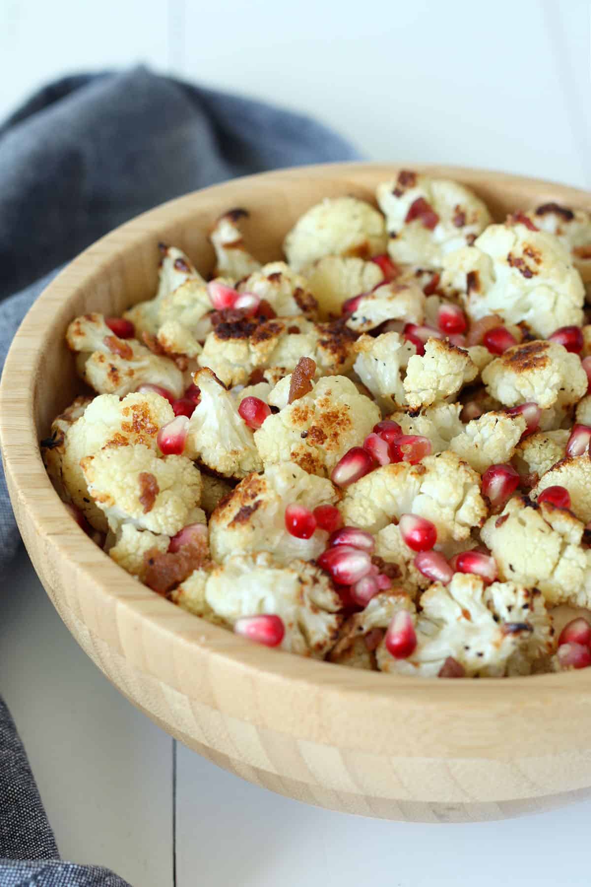 roasted cauliflower in a wood bowl with bacon pieces and pomegranate arils. 