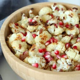 roasted cauliflower in a wood bowl with bacon pieces and pomegranate arils