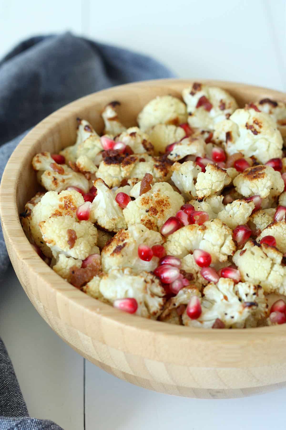 roasted cauliflower in a wood bowl with bacon pieces and pomegranate arils