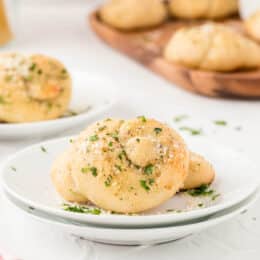 garlic knot on a white plate with garlic knots in the background on a wood cutting board