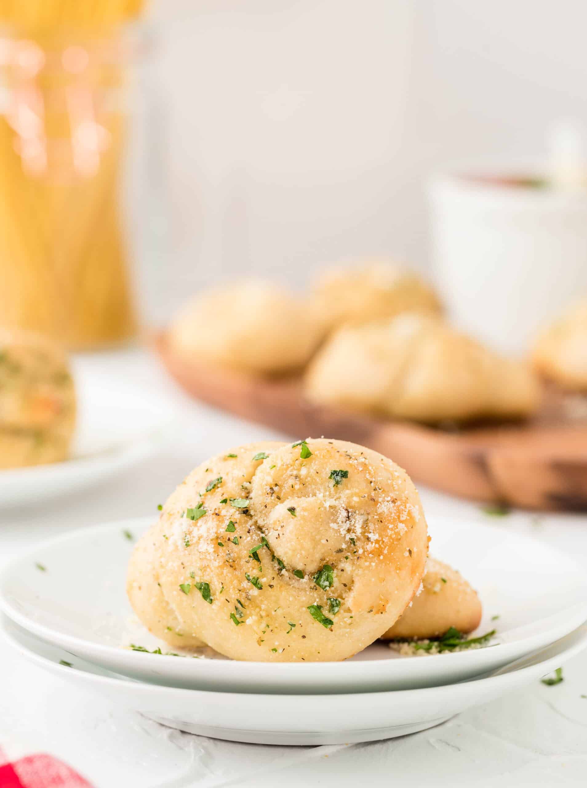 homemade garlic knot on a stack of white plates with more garlic knots in the background on a wood board