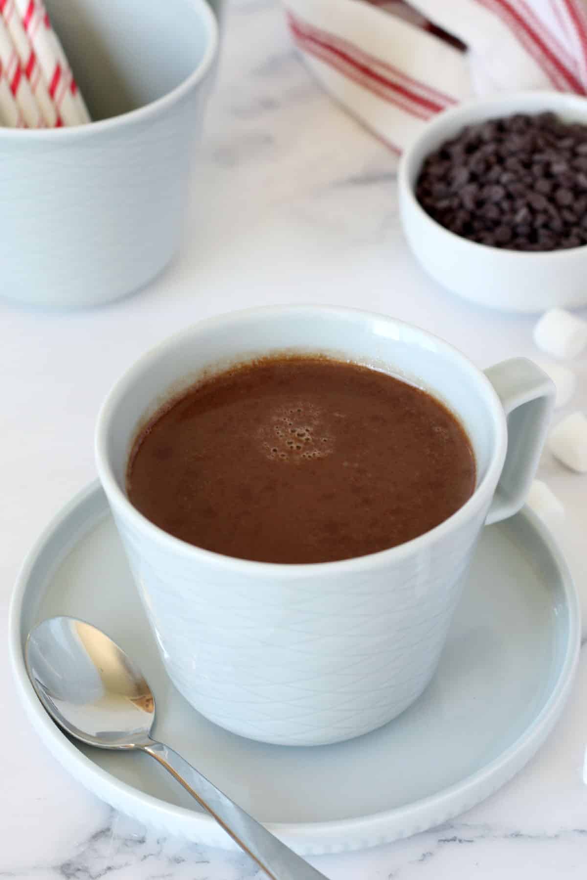 a mug of hot chocolate in a blue mug with a bowl of chocolate chips in the background