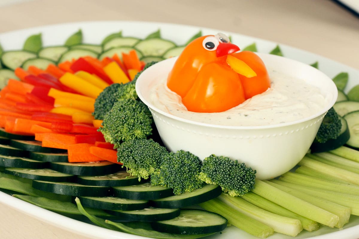 Sliced ​​cucumber, carrot and peppers arranged to look like turkey feathers with a bowl of ranch dip