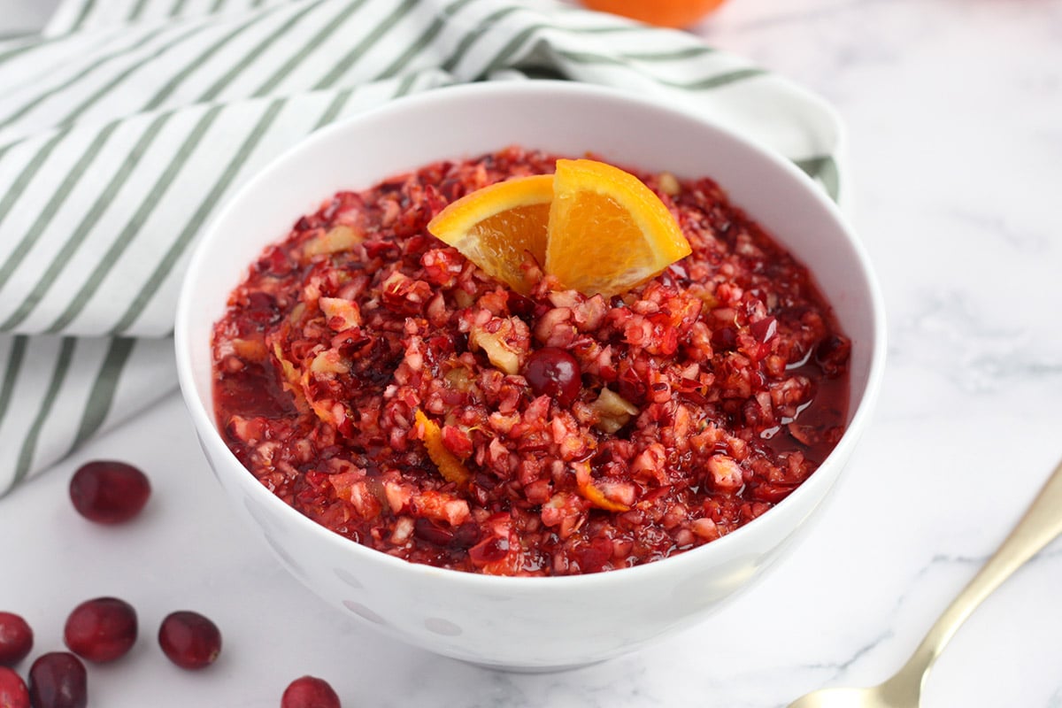 a bowl of cranberry orange relish in a white bowl with a striped towel in the background