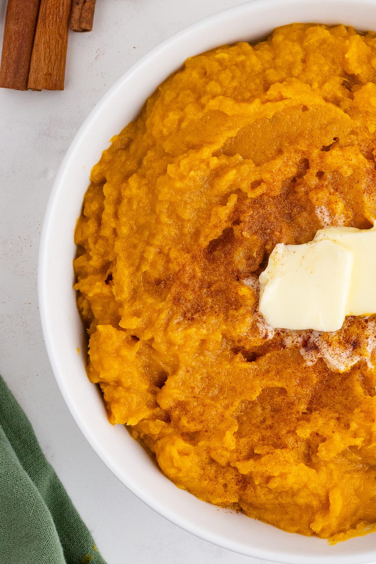 mashed sweet potatoes in a white dish with butter and cinnamon on top