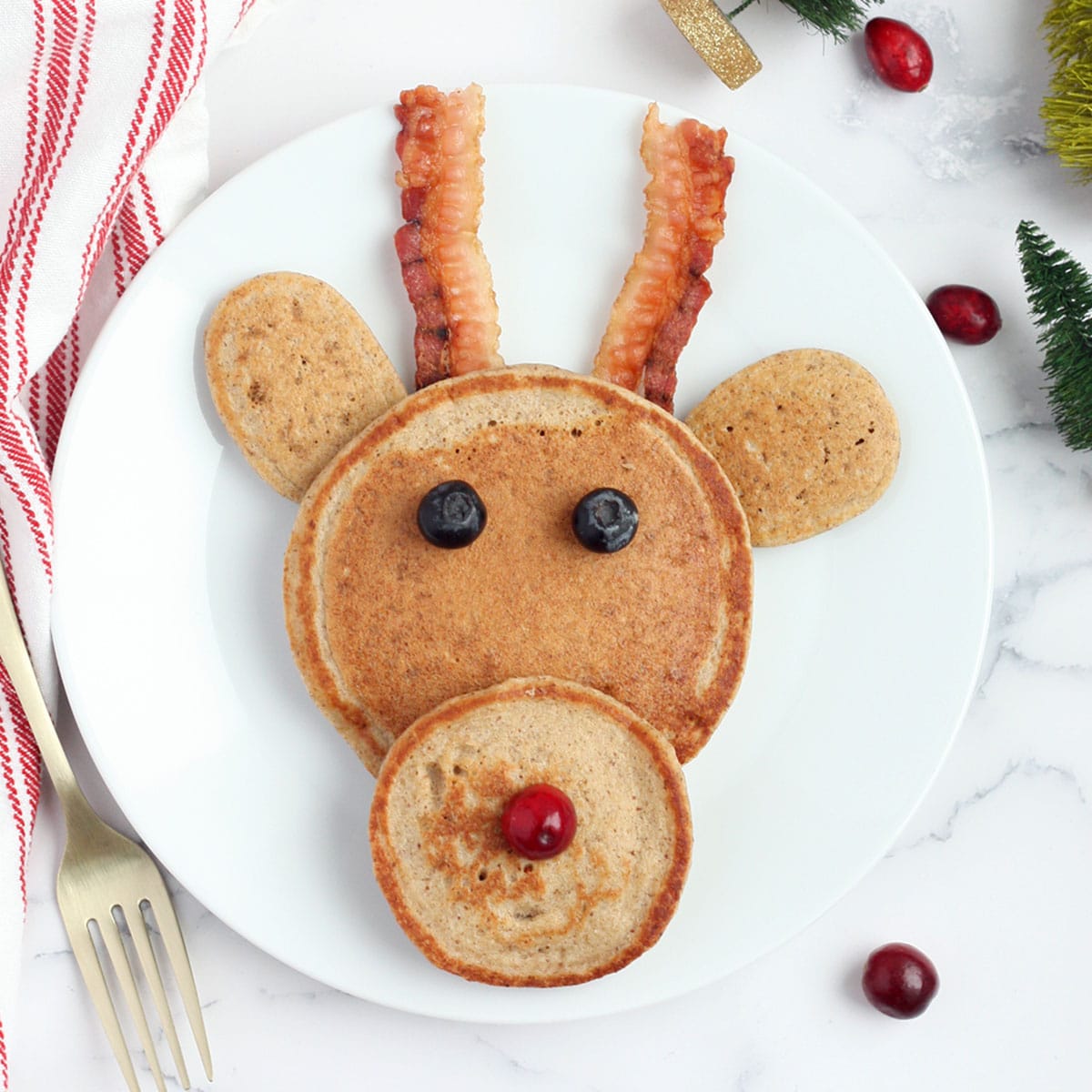 reindeer pancake on a white plate with bacon antlers and blueberry eyes