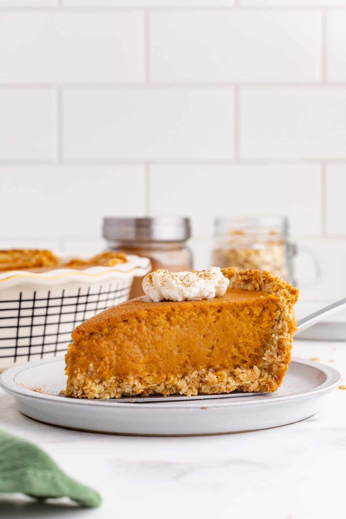 A slice of sweet potato pie with an oat crust, served with a whole pie against a background of whipped cream