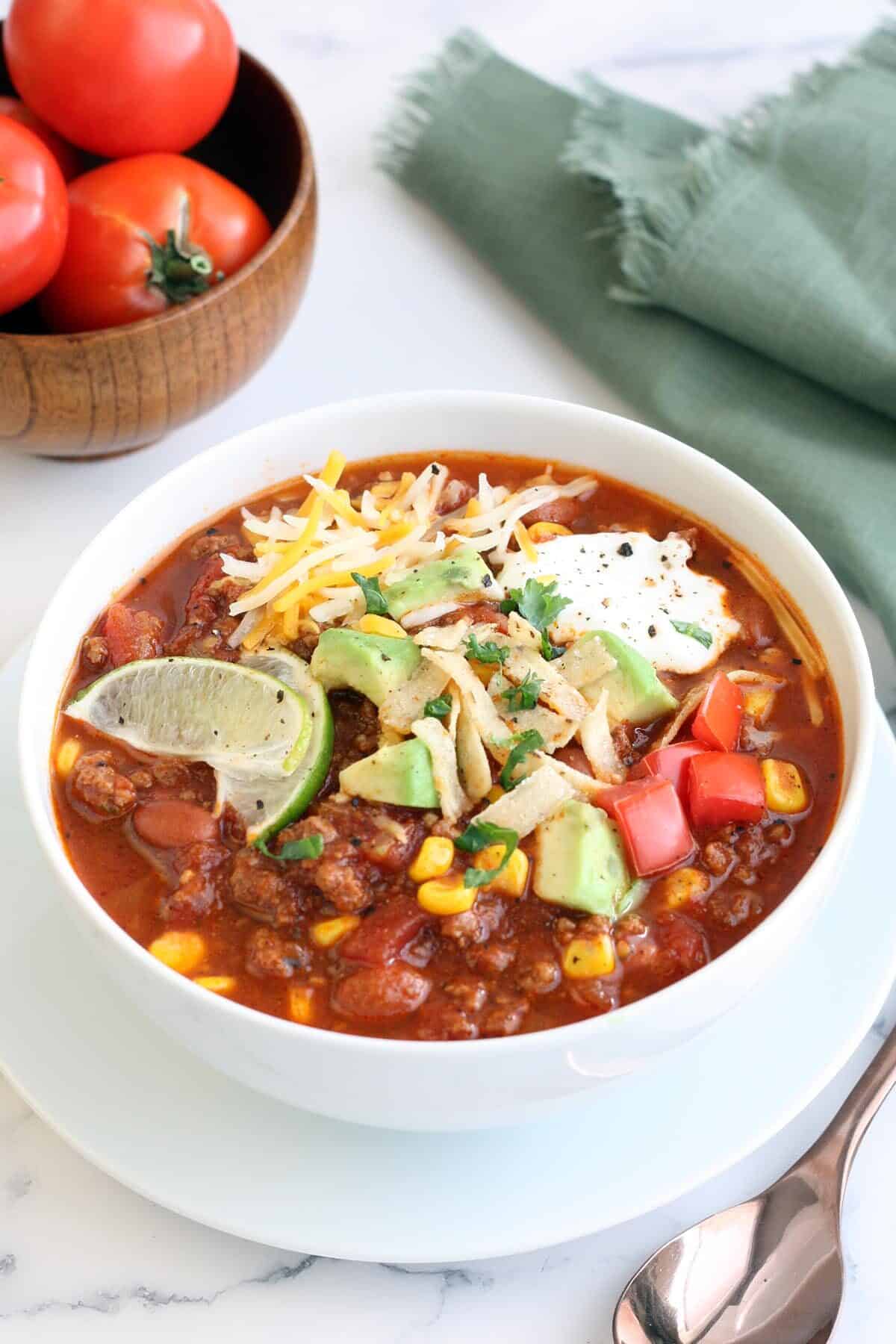 taco soup in a white bowl topped with avocado cheese and lime slices