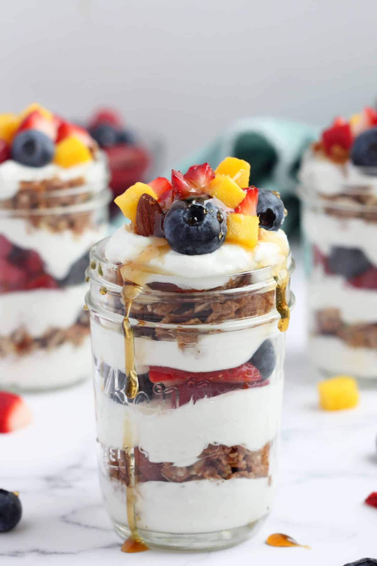 a yogurt parfait made with yogurt, fruit and granola drizzled with fresh maple syrup