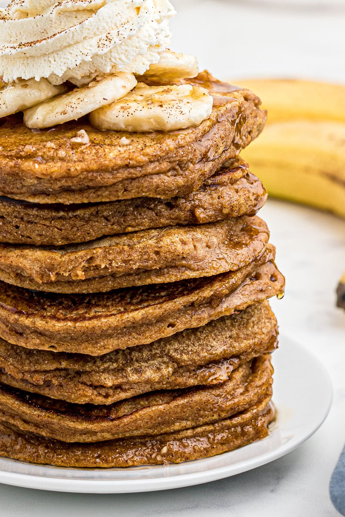 a close-up photo of sweet potato pancakes topped with bananas, whipped cream, cinnamon and chopped nuts