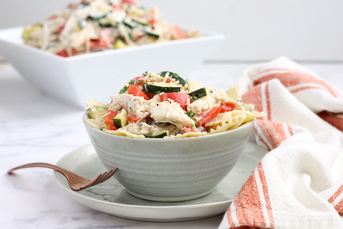 a serving bowl of creamy italian chicken served over bowtie pasta in a blue bowl