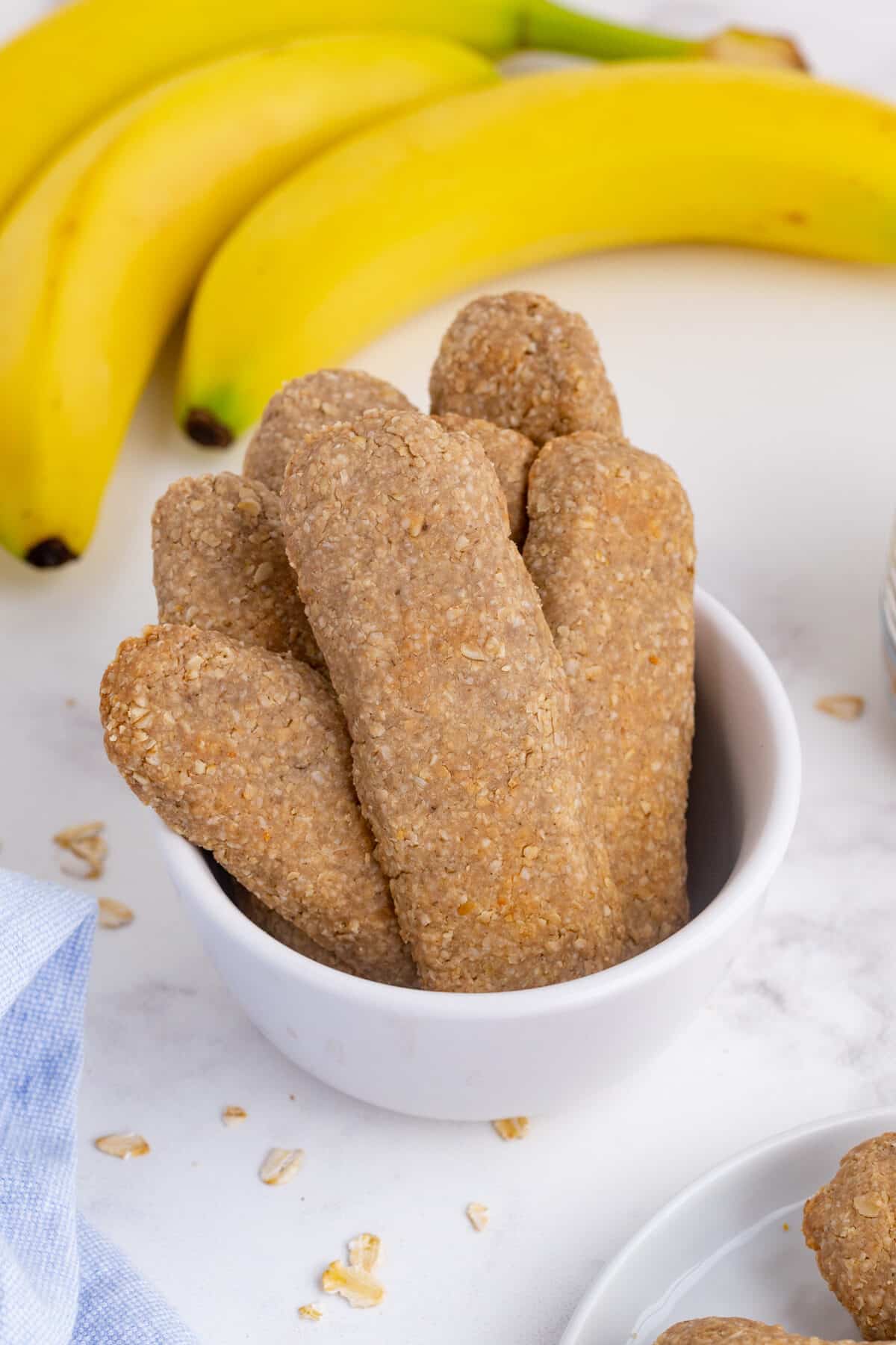 homemade teething biscuits in a white bowl with bananas in the background