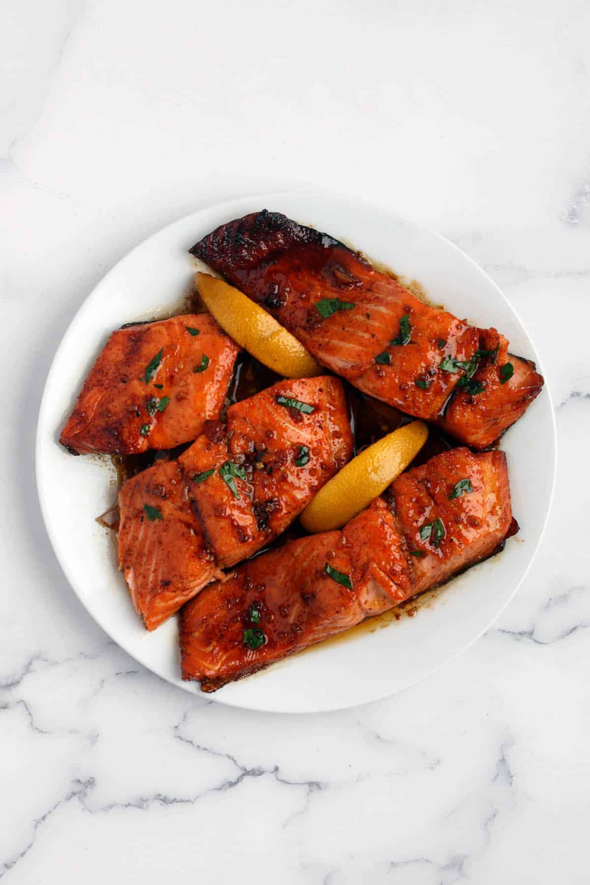 a white plate with fillets of honey garlic salmon and lemon wedges