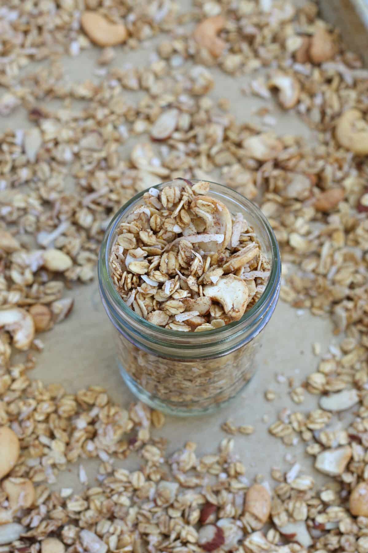 sugar free granola in a small mason jar on a baking sheet surrounded by granola