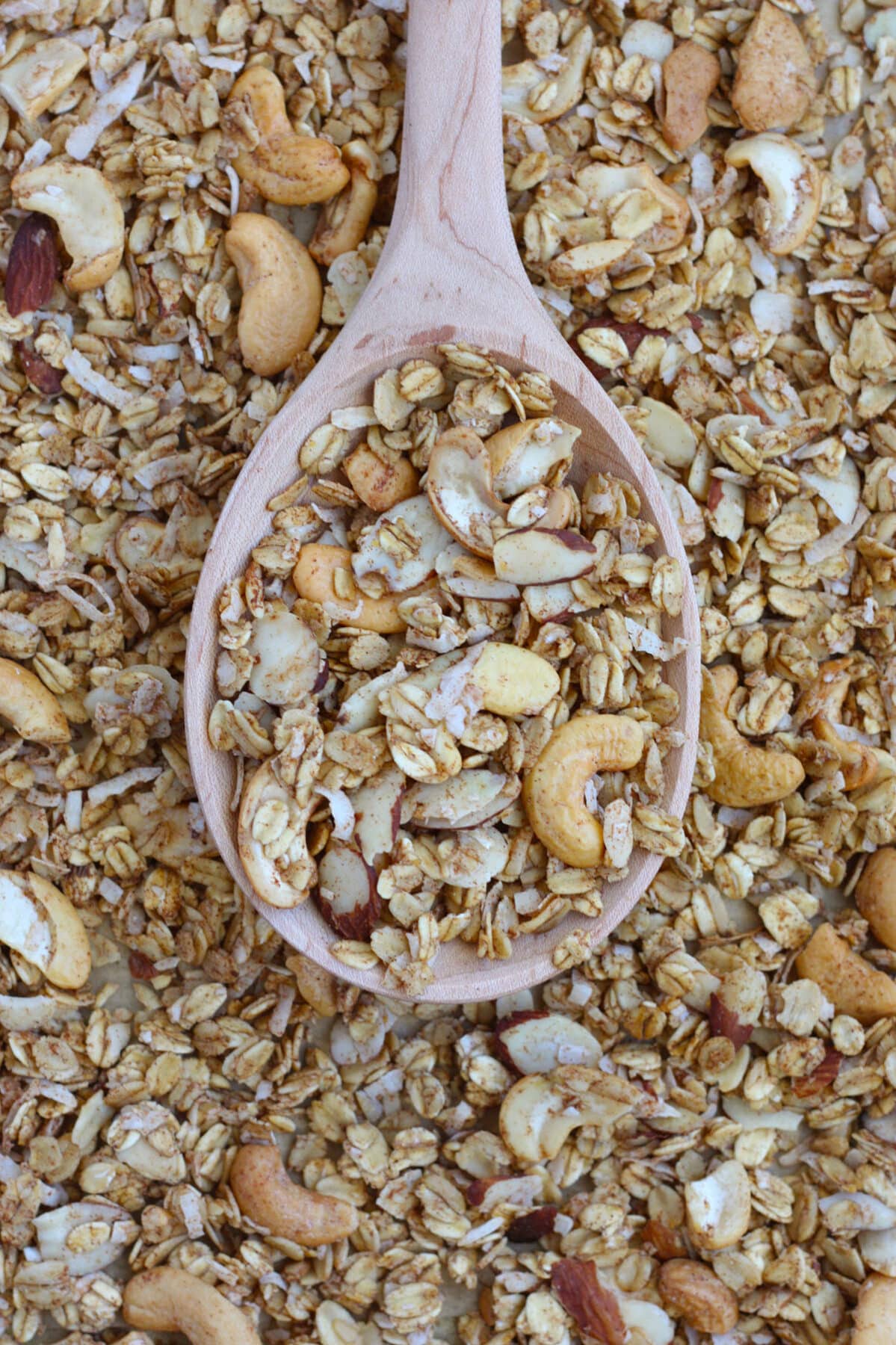 sugar free granola on a wooden spoon sitting on a baking sheet surrounded by granola