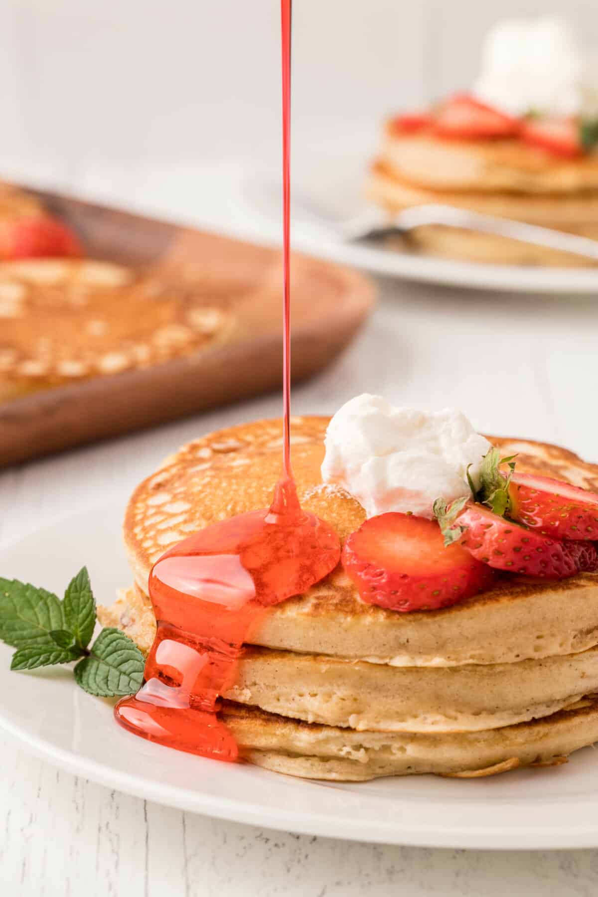 Stack of strawberry pancakes topped with whipped cream and drizzled with strawberry syrup