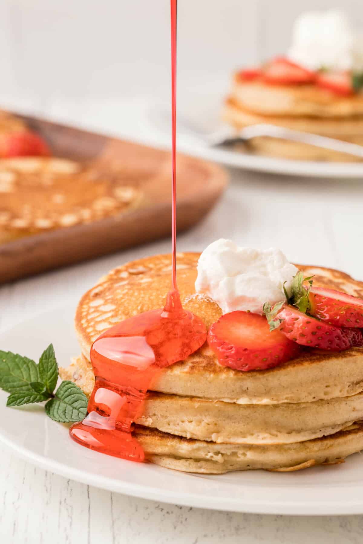 a stack of strawberry pancakes topped with whipped cream and drizzled with strawberry syrup