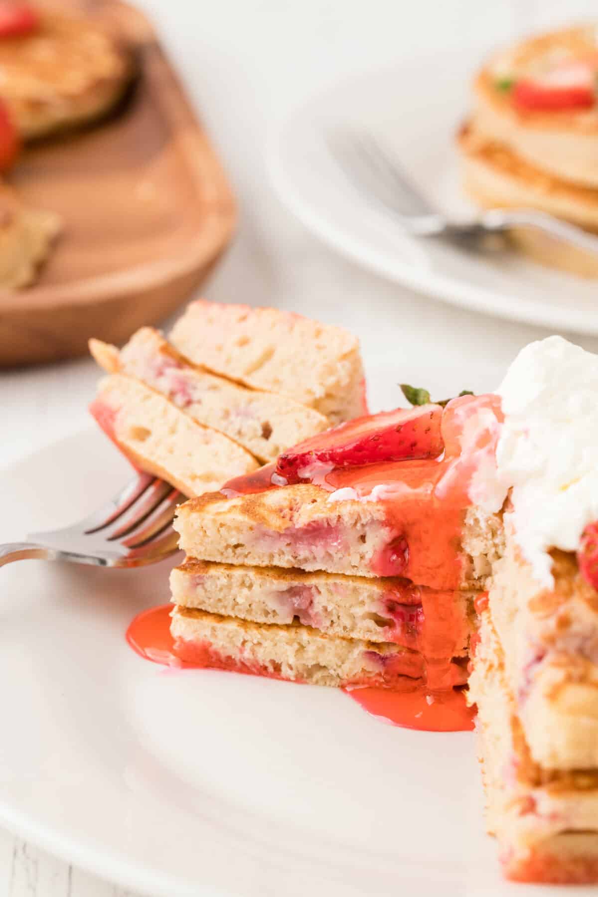 a stack of strawberry pancakes with a bite taken out