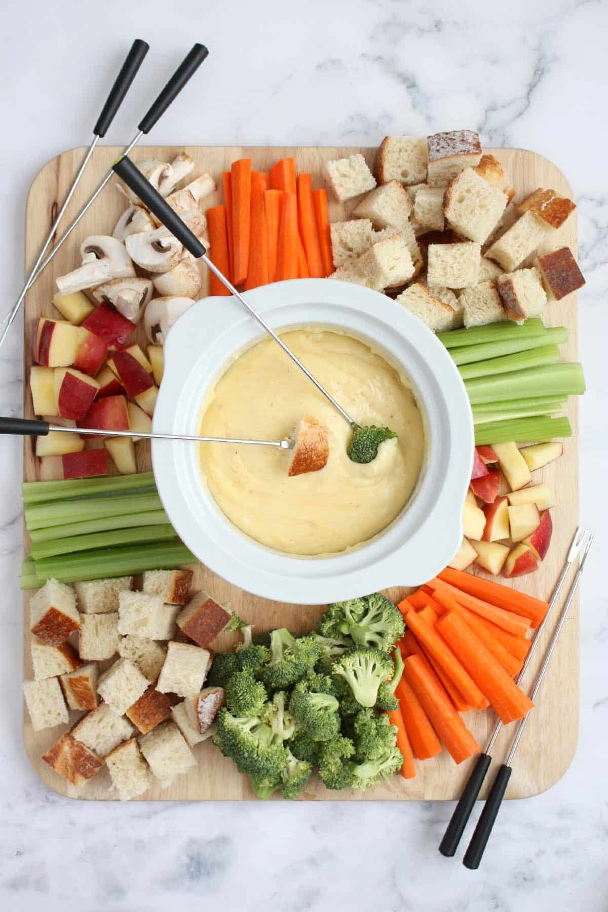 a fondue board with fruit, veggies, bread, and cheese fondue with fondue forks