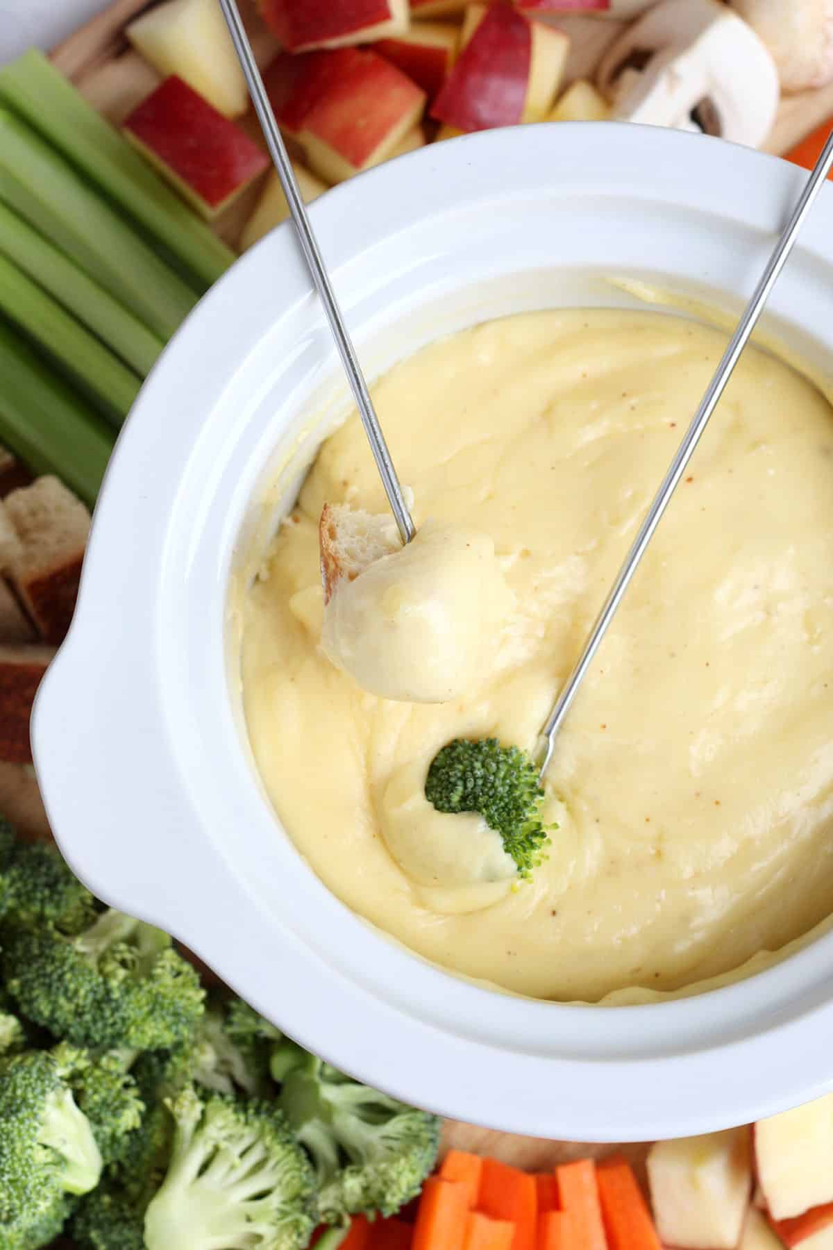 cheese fondue in a white ceramic pot with assorted fruits and veggies