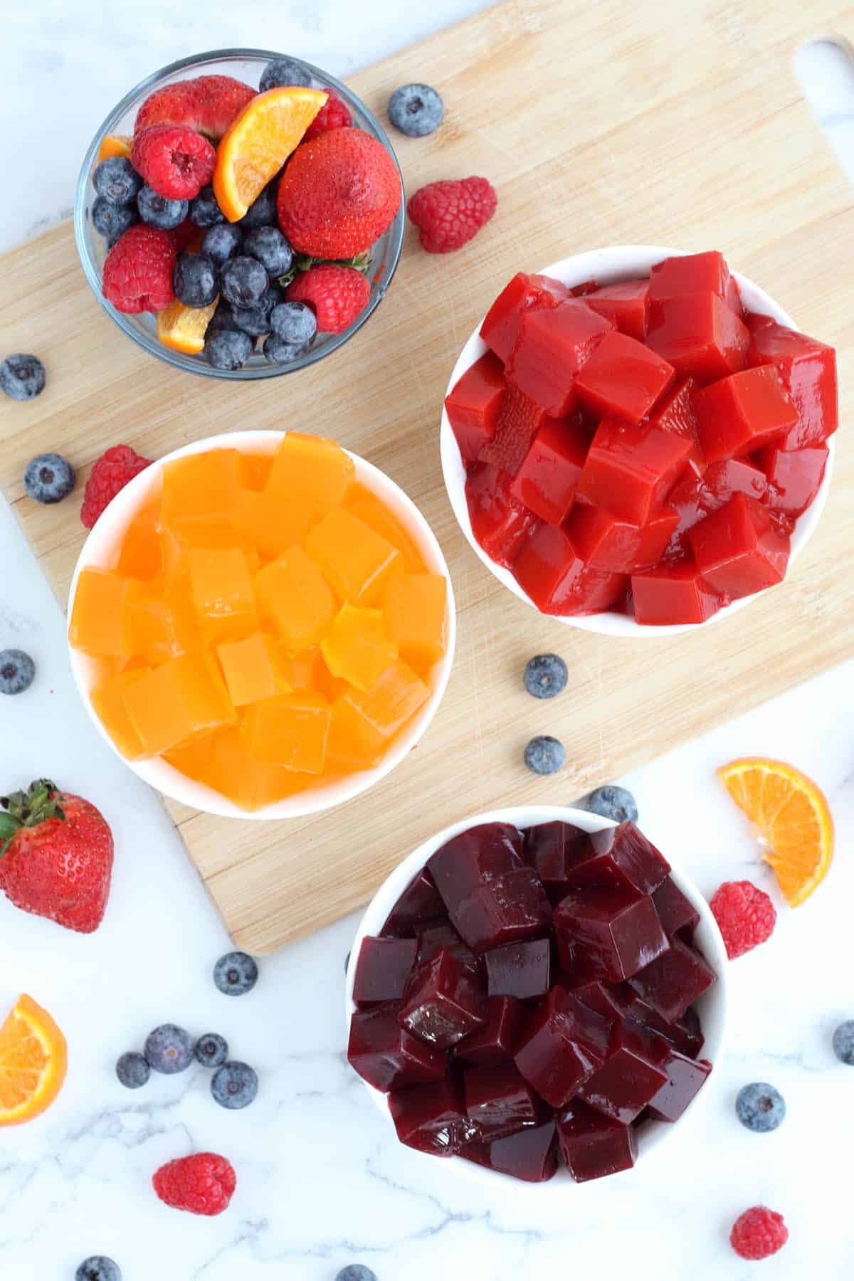 Bowls of homemade jello on a wooden board with fresh fruit