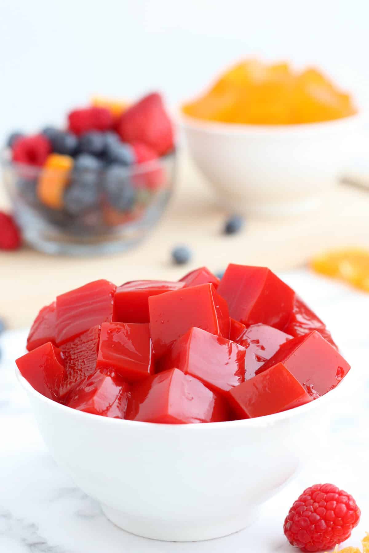 red homemade jello in a white bowl with fresh raspberries