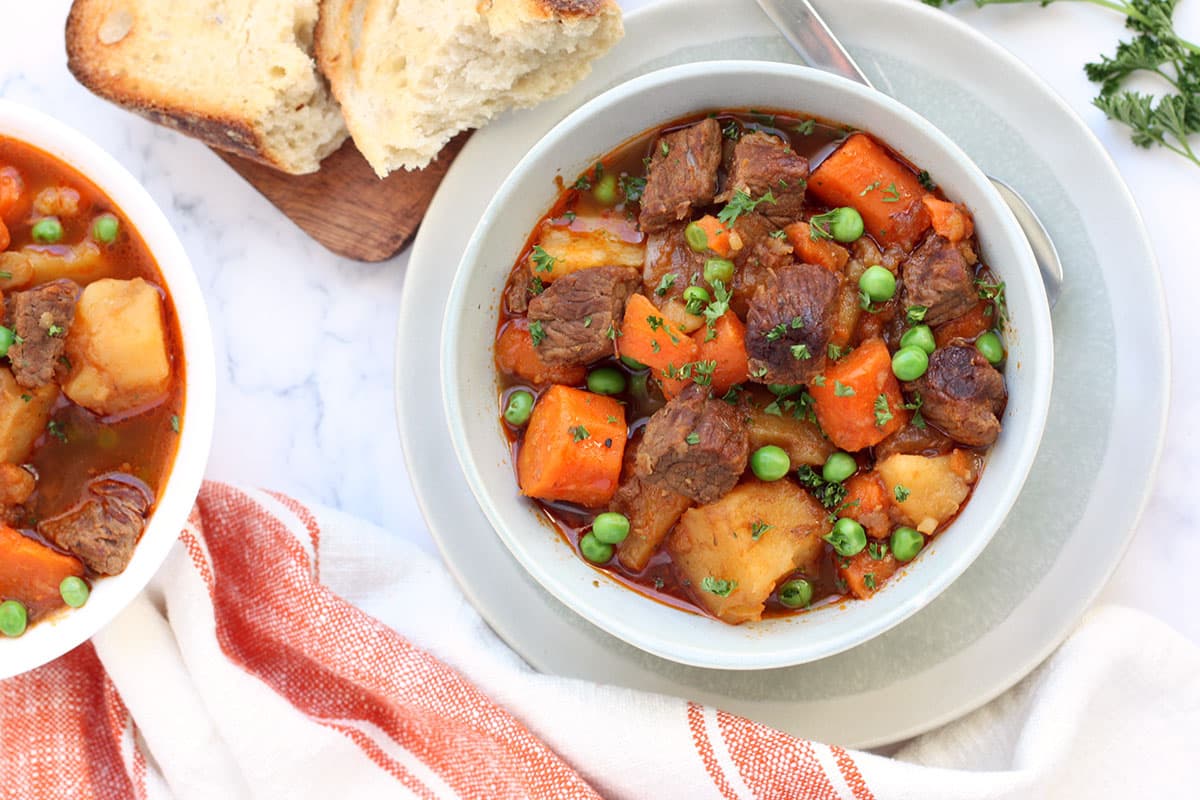 overhead view of a two bowls of beef stew made in the instant pot with crusty bread in the background