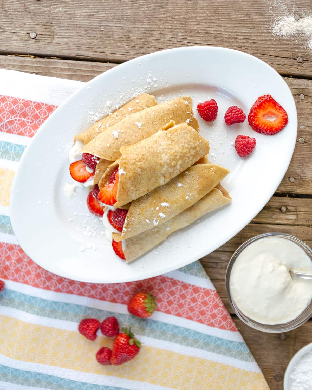 overhead view of strawberry crepes filled with fresh strawberries and raspberries and a cream filling on a white plate