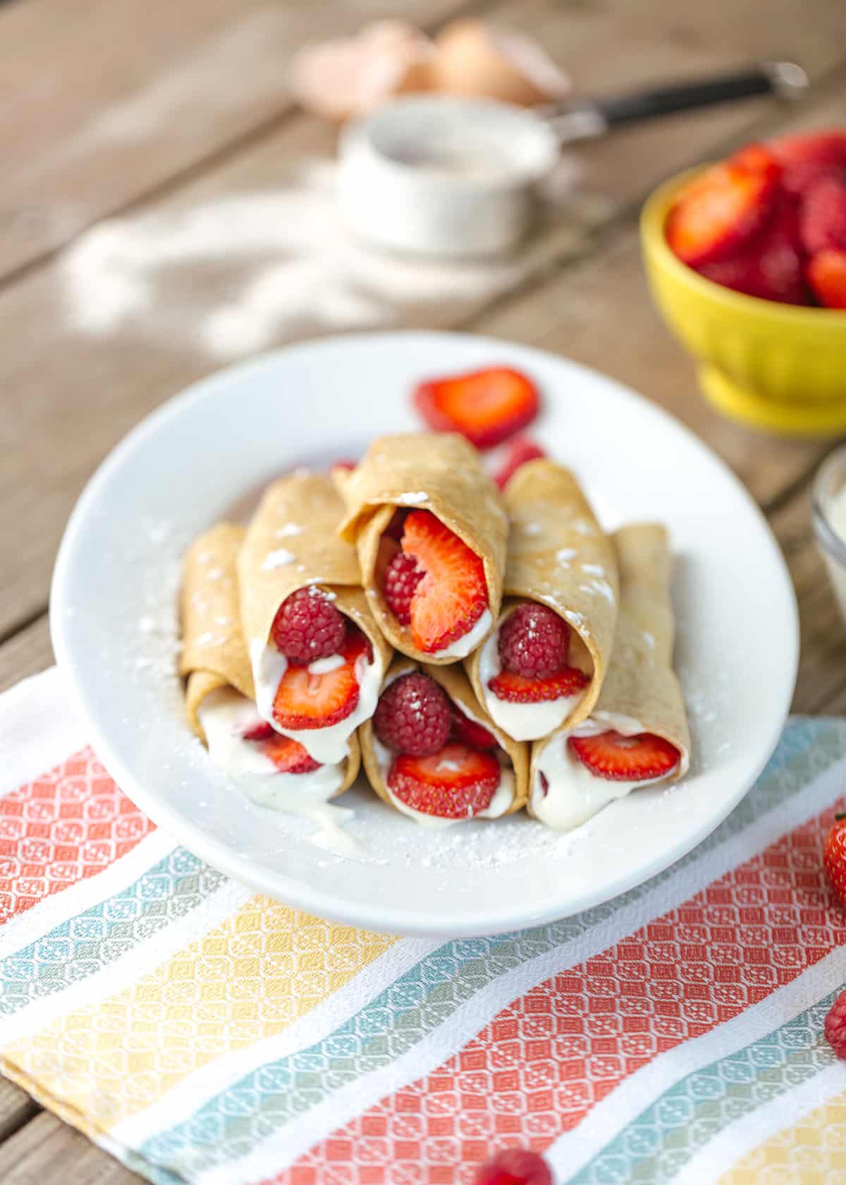 a plate of strawberry crepes filled with fresh strawberries and a creamy sauce on a colorful serviette