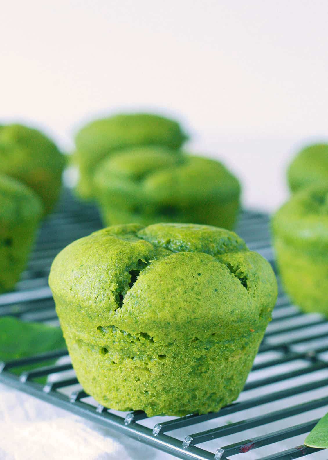 spinach muffin on a cooling rack with spinach muffins in the background full of spinach 