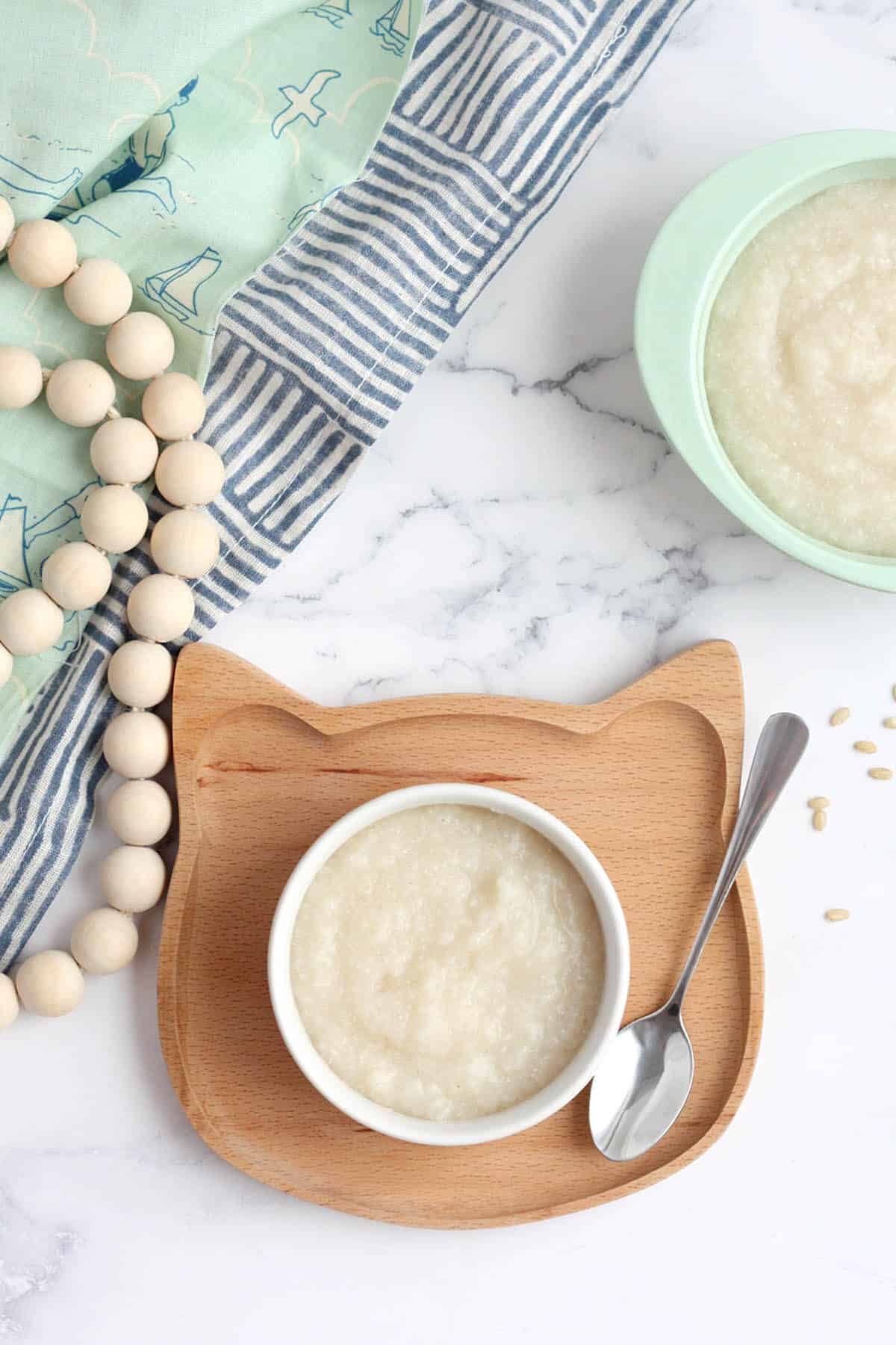 a bowl of baby cereal on a wooden cat plate with wooden beads in the background